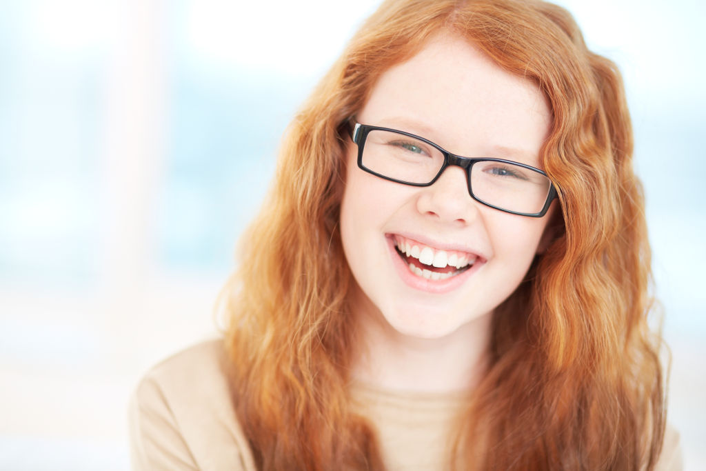 Teenage girl in eyeglasses looking at camera and laughing